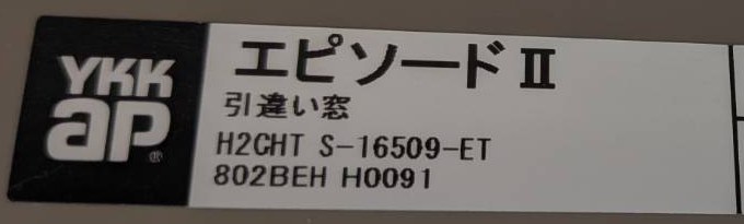YKK APのシールの左側。ロゴの右の白い欄に「エピソードⅡ」「引違い窓」と、その下に品番「H2CHT S-16509-ET」が印字されている。